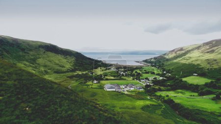 Écosse village photo aérienne : montagne, vallée verdoyante. Ville écossaise à flanc de colline avec lac de mer, ruines du château. Loch Ranza resort and distillery in Arran Island, Royaume-Uni. Tournage de séquences