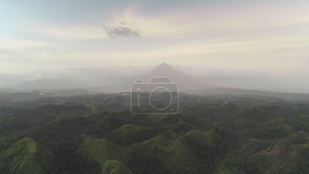 Jungle hills aerial at cloudy sky with Mayon Mount. Green plants at dusk summer day. Epic nature scenery of Legazpi city, Albay province, Philippines, Visayas archipelago, Asia. Cinematic drone shot