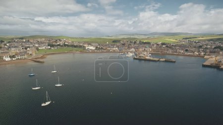 Yachts regatta at pier town cityscape aerial. Buildings at traffic road with cars. Wharf with water transport at ocean bay. Scotland Campbeltown city attraction at summer cruise on sailboats race