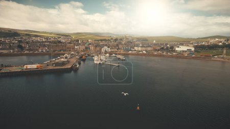 Sun pier town cityscape aerial. Seagull flight over ocean bay. Yachts, ships at marina. Historic buildings architecture landmark at urban streets of Campbeltown city, Scotland. Cinematic seascape
