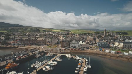 Sun marina with ships, yachts aerial. Epic cityscape of harbor town of Campbeltown, Scotland, Europe. Downtown streets with traffic highway. European urban scenery. Scottish seascape at summer day