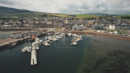 Sun dock with yachts aerial. Summer cityscape of port Campbeltown city, Scotland, Europe. Downtown streets with modern buildings. European urban scenery. Scottish seascape at sunlight
