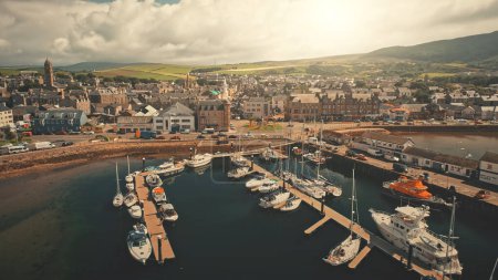 Sun harbor town cityscape at marina aerial. Downtown streets at sunlight traffic road. Green hills landscape admist modern buildings. Campbeltown urban scenery. Scotland nobody nature at summer day