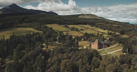 Scotlands mountains, old castle aerial panning shot: designed landscapes of garden and parks near building. Beautiful woods, hills, valleys in horizon at summer day. Dramatic scenery view