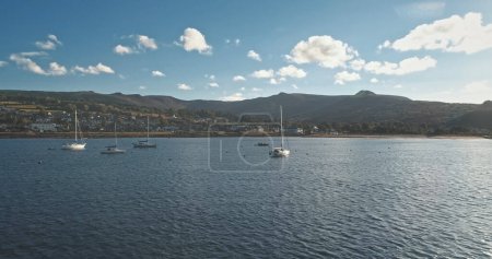 Regatta on luxury yachts aerial. Sail boats cruise at ocean bay in Brodick harbor, Arran Island, Scotland, Europe. Cinematic seascape of summer vacation sunny day. Panorama drone shot