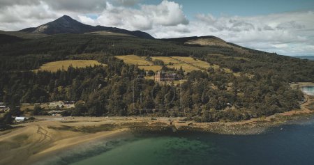 Scotlands ocean coast landscape aerial view: forests, valleys, hills. Brodick castle - historical ancient building in Arran Island. Road with riding cars shot