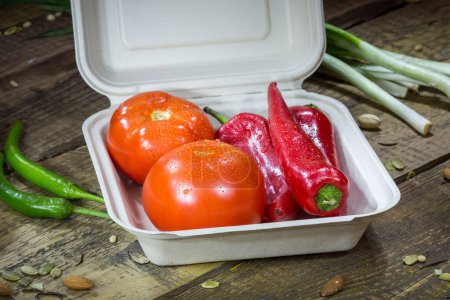 Téléchargez les photos : Paprika, tomatoes and greens in an disposable container on a wooden background - en image libre de droit