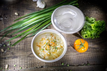 Téléchargez les photos : Soup with spaghetti in a disposable bowl on rough wooden boards in dramatic light - en image libre de droit