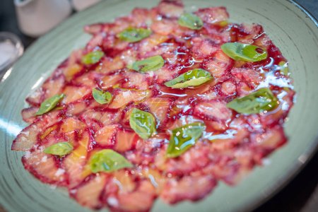 Photo for Portion of salmon carpaccio with fresh basil and sauce on a ceramic dish on a wooden table - Royalty Free Image