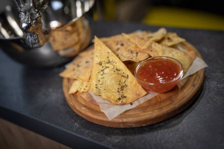 Foto de Tortillas de nachos mexicanos con chile con carne en un plato redondo de madera sobre una losa de piedra oscura con platos de plata - Imagen libre de derechos