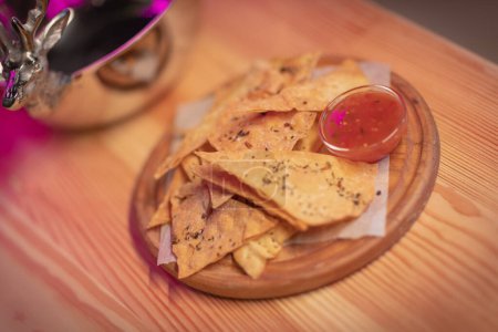 Photo for Mexican nachos tortilla chips with chili con carne on a round wooden plate on a wooden slab with silver dishes - Royalty Free Image