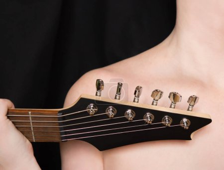 Foto de Fragmento de una guitarra eléctrica delante del cuerpo femenino. Estética de la luz y la sombra, cultura musical - Imagen libre de derechos