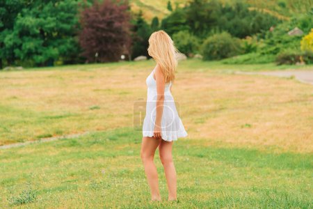 Foto de Día cálido de verano. La mujer camina descalza en el parque con un vestido blanco corto. Paisaje rural. Sin cara, vista desde atrás.. - Imagen libre de derechos