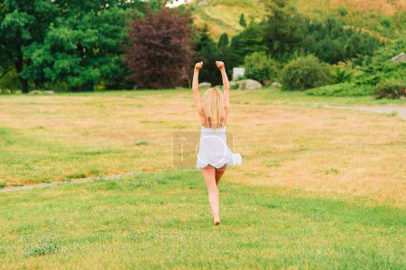Photo for Summer warm day. Woman walks barefoot in the park in a short white dress. Rural landscape. No face, view from the back. - Royalty Free Image
