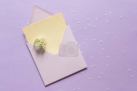 Leere Grußkarten-Attrappe. Leicht leeres Blatt Papier-Attrappe in einem Umschlag. Weiße Blumen auf violettem Papier Hintergrund. Flach lag er. Hochzeit, Geburtstag Stillleben Szene.