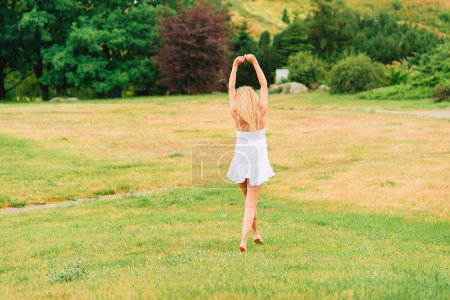 Photo for Summer warm day. Woman walks barefoot in the park in a short white dress. Rural landscape. No face, view from the back. - Royalty Free Image