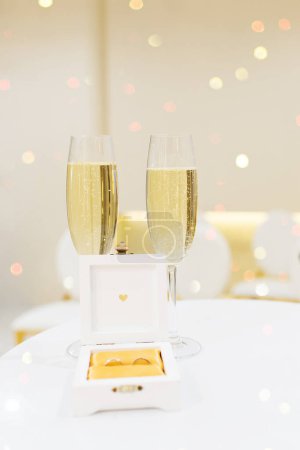 Foto de Dos copas de champán en la mesa, caja con anillos de boda. Luces Bokeh en el fondo. - Imagen libre de derechos