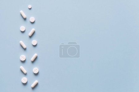 Téléchargez les photos : Des pilules blanches éparpillées sur une table bleue. Maquette pour des offres spéciales comme la publicité, fond web ou d'autres idées. Concept médical, pharmacie et soins de santé. Espace de copie. Espace vide pour le texte ou le logo - en image libre de droit