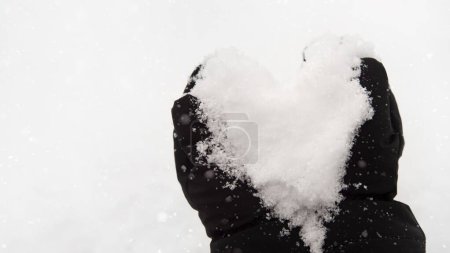 Foto de Corazón hecho de nieve. Las manos del hombre con guantes sostienen una nieve blanca en un bosque. Copos de nieve. Paisaje invierno. - Imagen libre de derechos