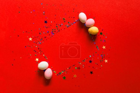 Happy easter decor concept. Festive bright red background with glitter and sparkles, chocolates in the form of Easter eggs. Copy space, flat lay, top view. Blank greeting card, invitation mockup