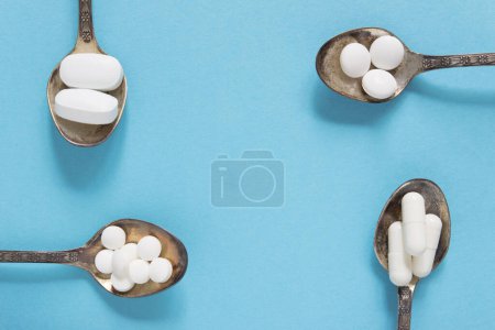 Téléchargez les photos : Ensembles de différentes pilules blanches dans une cuillère en argent sur fond bleu. Maquette pour des offres spéciales comme la publicité, fond web ou d'autres idées. Espace de copie - en image libre de droit