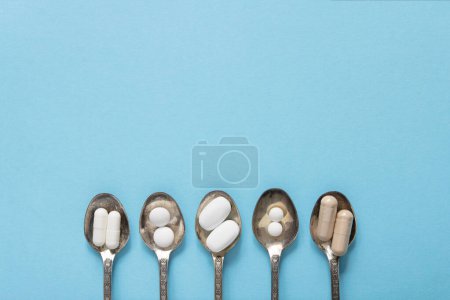 Téléchargez les photos : Ensembles de différentes pilules blanches dans une cuillère en argent sur fond bleu. Maquette pour des offres spéciales comme la publicité, fond web ou d'autres idées. Espace de copie - en image libre de droit