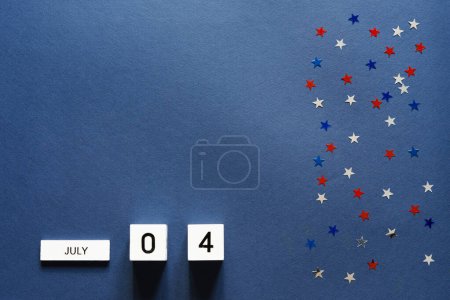 Téléchargez les photos : Fête de l'indépendance américaine, vue du dessus sur cubes en bois calendrier 4 juillet sur fond bleu avec des étoiles confettis - en image libre de droit