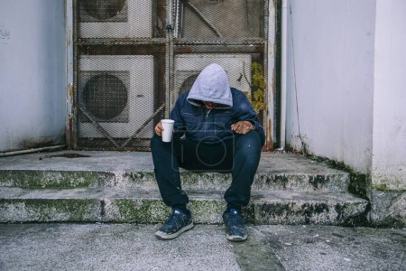 Foto de Sad homeless man begs for money at the street. - Imagen libre de derechos