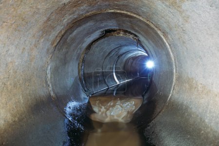 Dirty sewage flowing in round underground sewer tunnel.