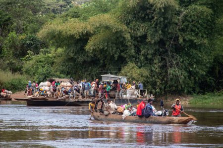 Foto de Transporte de personas a través del río Mbari en canoas hechas localmente y en ferry. Pasajeros vestidos de colores, transportando variedad de bienes comprados en el mercado local en el día de fin de semana - Imagen libre de derechos