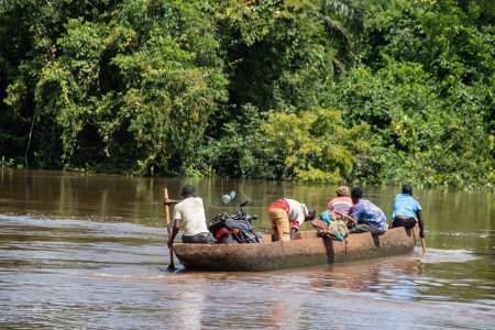 Foto de Transporte de personas a través del río Mbari en canoas hechas localmente y en ferry. Pasajeros vestidos de colores, transportando variedad de bienes comprados en el mercado local en el día de fin de semana - Imagen libre de derechos