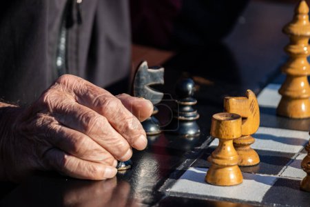Hände älterer Rentner mit Schachfiguren im öffentlichen Park in Belgrad, schöner sonniger Tag