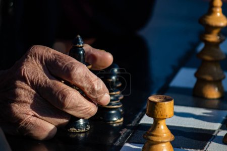 Hände älterer Rentner mit Schachfiguren im öffentlichen Park in Belgrad, schöner sonniger Tag