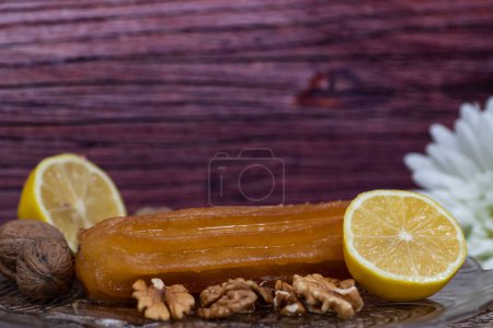 gâteau sucré turc appelé tulumba, servi dans une assiette avec des tranches de citron et de noix autour, sur une table en bois massif