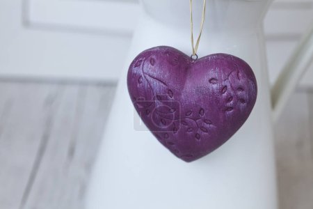 Foto de Corazón púrpura colgando de una jarra blanca sobre fondo de madera rústica - Imagen libre de derechos