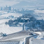 View of rural road among hills and vineyards covered with snow in Piedmont, Northern Italy.