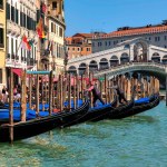 VENICE, ITALY - APRIL 06, 2023: Gondolas moored on Grand Canal in front of the Rialto Bridge in Venice - famous italian city built on 118 small islands separated by canals, popular travel destination.