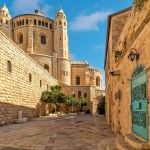 View of narrow street among ancient walls as Dormition Abbey under blue sky on background in old city of Jerusalem, Israel.