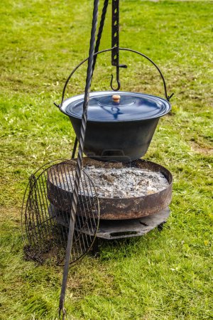 Photo for Dutch oven with campfire and grill grate on a green meadow - Royalty Free Image