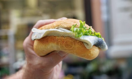 Man's hand holds fish sandwich with herring.