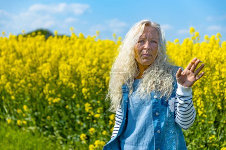 Ältere Frau raucht Zigarette im Rapsfeld mit gelben Blüten