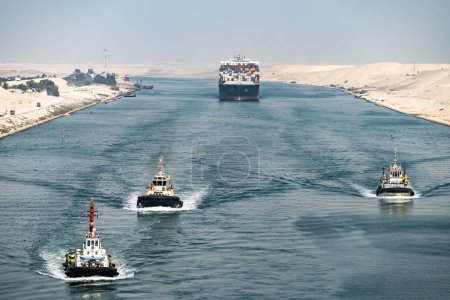 Huge cargo ships with pilot boats navigate by Suez Canal, Egypt. Concept of transportation and logistics.