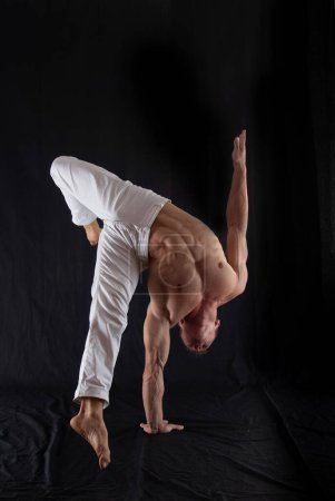 Circus artist keeps balance on one hand isolated on a black background. Concept of individuality, creativity and self-confidence.