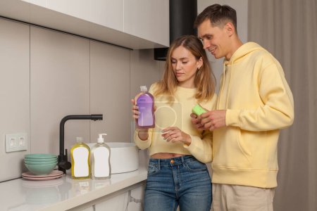 Téléchargez les photos : Détroit de couple, homme et femme en vêtements jaunes tenant le lave-vaisselle liquide coloré avec étiquette vierge - en image libre de droit