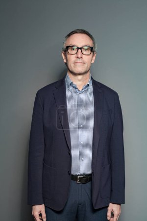 Téléchargez les photos : Homme d'affaires mature en costume bleu foncé et chemise à carreaux sur fond mural gris - en image libre de droit
