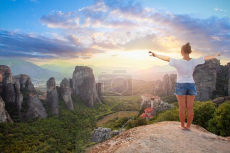 Photo for Travel in Greece. Young woman standing on a rock overlooking Meteora at sunset - Royalty Free Image