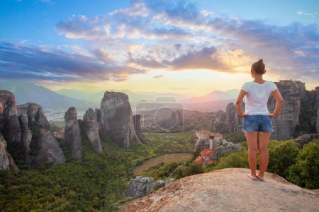 Photo for Young woman in white t-shirt standing in front of Greece Meteora mountains, monastery and village in the background - Royalty Free Image