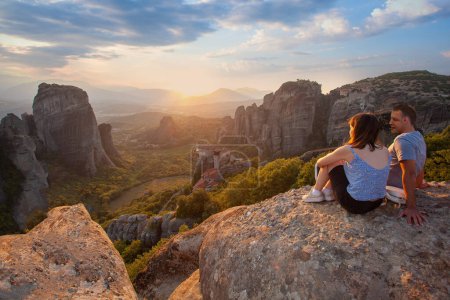 Photo for Love couple sitting on a rock overlooking Meteora at sunset. Travel in Greece. - Royalty Free Image
