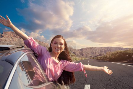 Carefree brunette woman having fun outside open window car against road and mountain background. People lifestyle relaxing as traveler on road trip in holiday vacation, travel concept