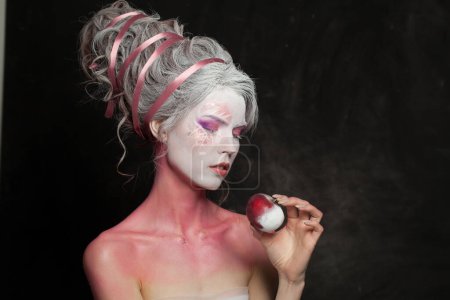 Téléchargez les photos : Magicien femme avec art corporel créatif tenant res portrait pomme enneigée. Maquillage carnaval ou Halloween - en image libre de droit